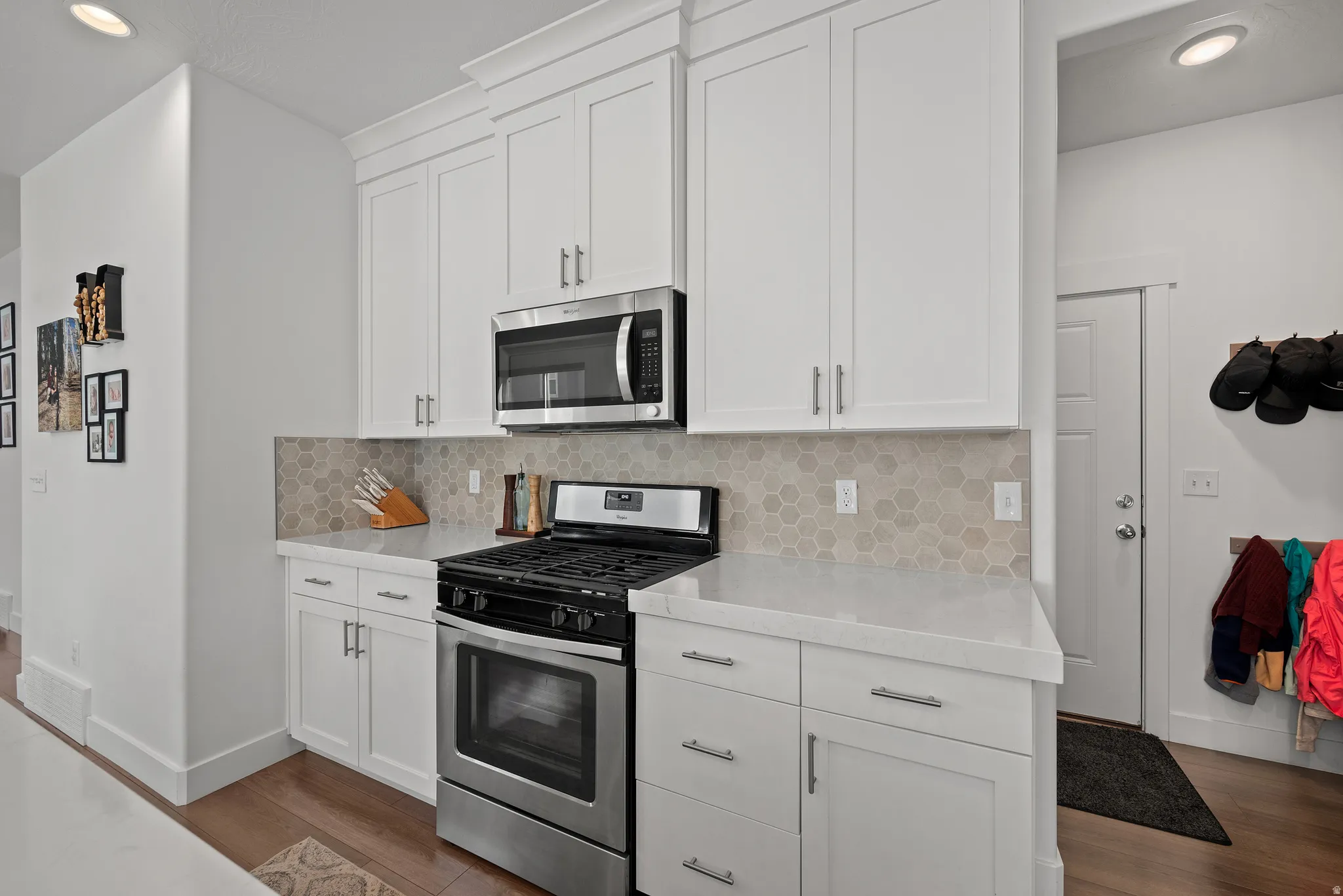 White shaker cabinetry with crown molding, stainless steel microwave, gas range, light-toned hexagon tile backsplash, and light-toned countertops