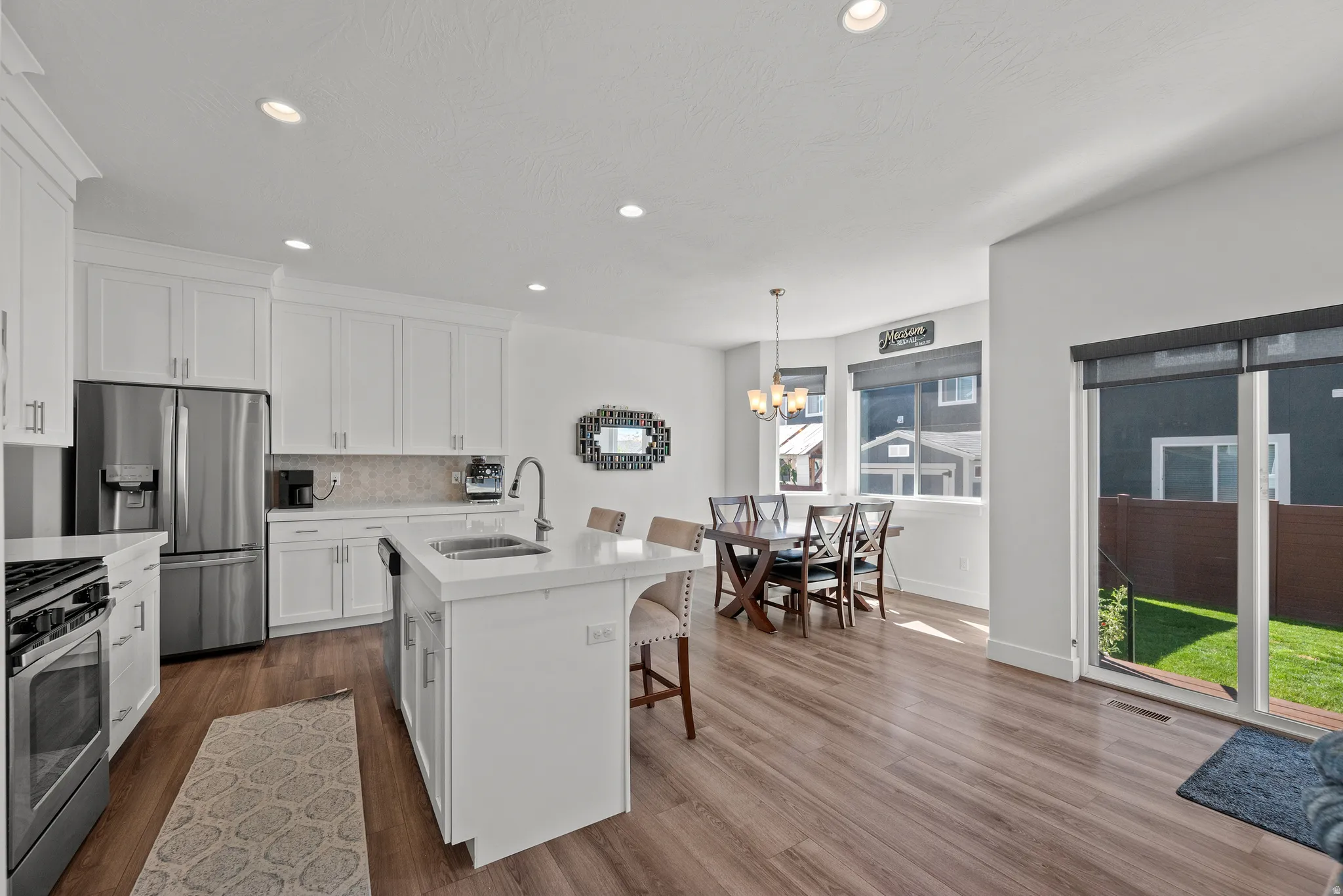 Kitchen featuring white cabinetry, stainless steel appliances, a center island with sink, wood-finish flooring, and a sliding glass door to the backyard