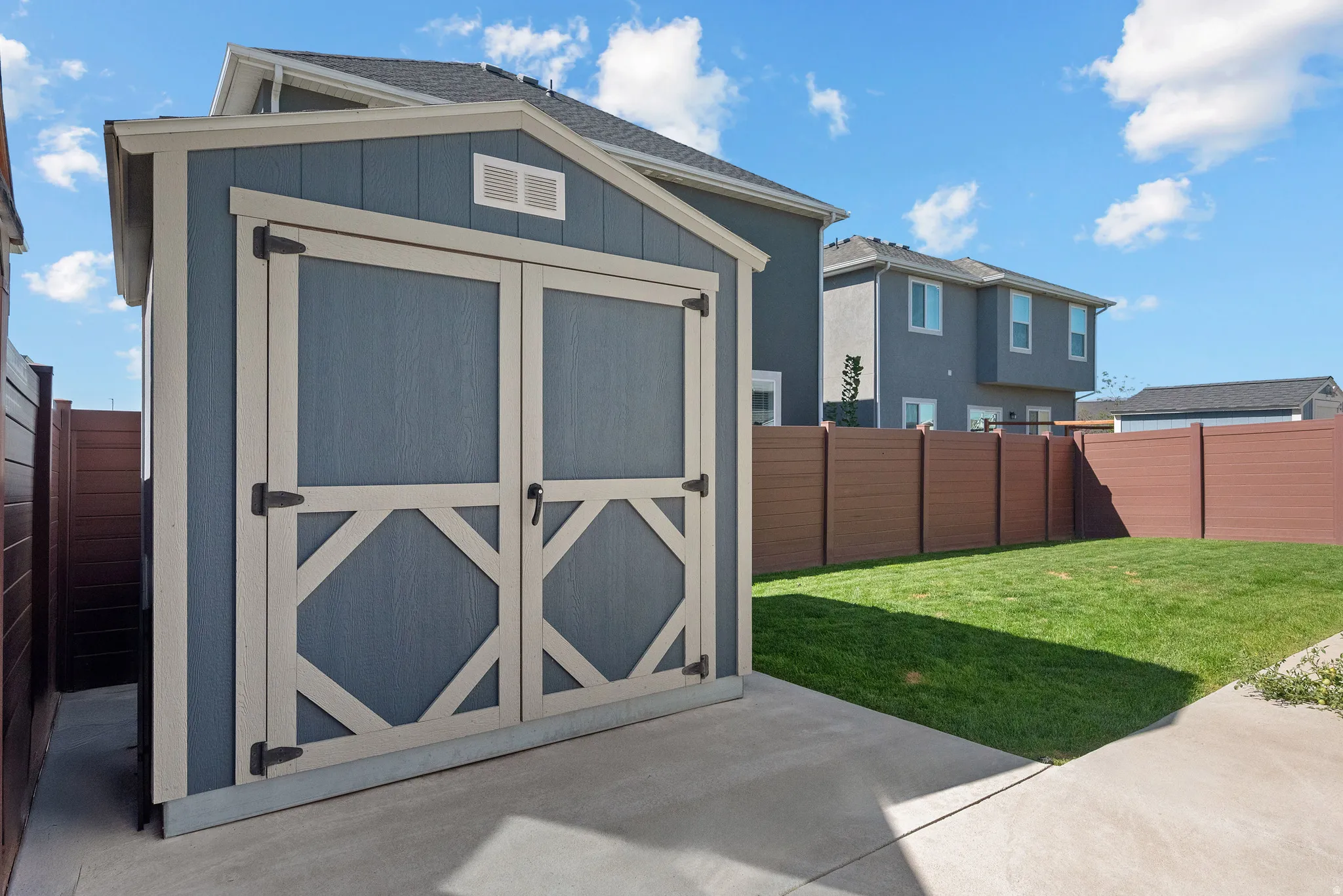 Enclosed backyard with a storage shed, concrete patio, and a manicured lawn, bordered by a brown privacy fence