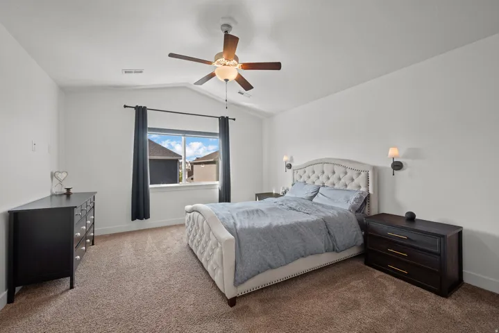Vaulted ceiling with a ceiling fan, carpeted flooring, and a window with dark curtains