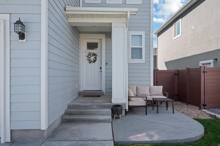 Light blue horizontal siding, white trim, covered porch entry, concrete patio, and brown privacy fence