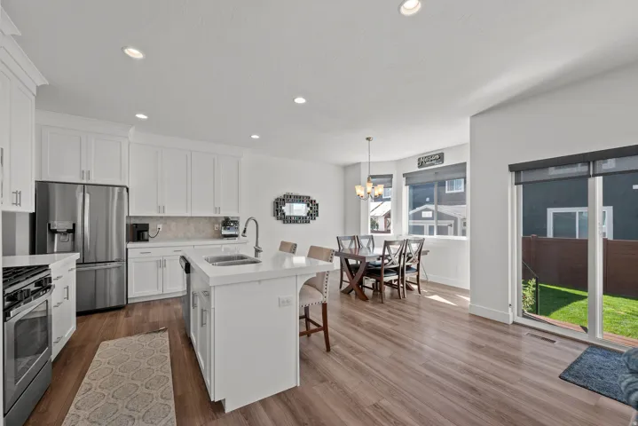 Kitchen featuring white cabinetry, stainless steel appliances, a center island with sink, wood-finish flooring, and a sliding glass door to the backyard
