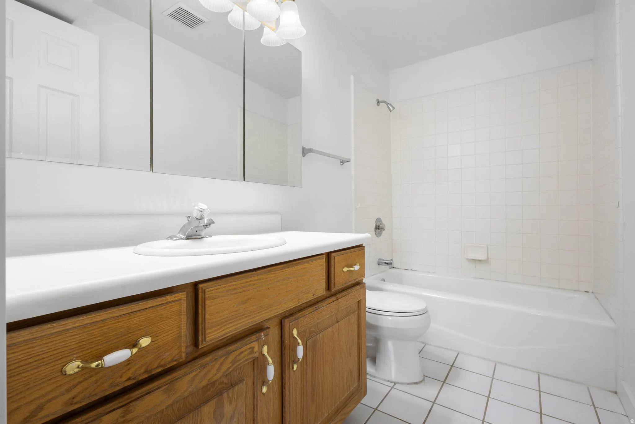 Bathroom featuring a wood-finish vanity with white countertop, integrated sink, and triple mirrored medicine cabinet