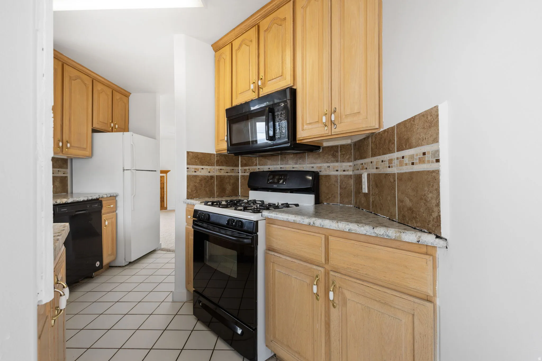 Kitchen featuring wood-finish cabinetry, tile backsplash, built-in microwave, and range