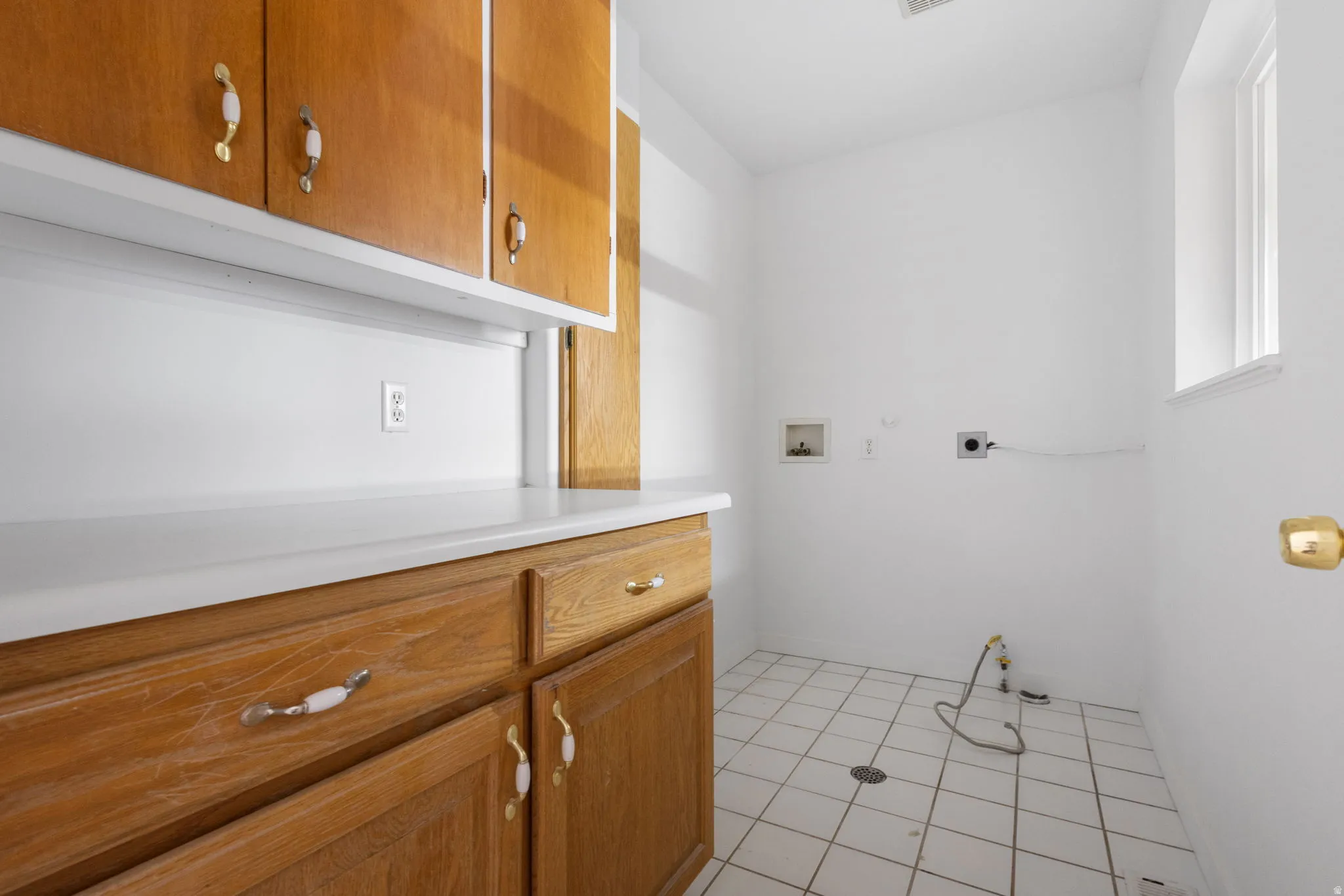 White tile flooring, wood-finish cabinetry, white countertops, built-in window, and overhead lighting
