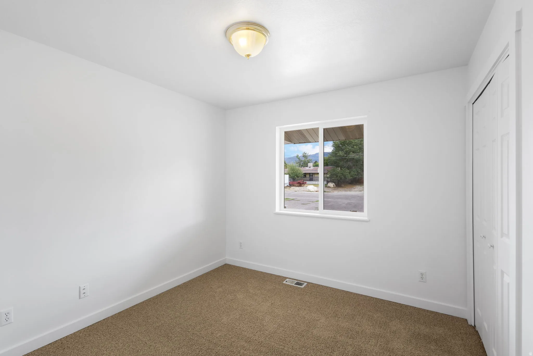 White interior walls, brown carpet flooring, single-pane window, and a white bi-fold closet door