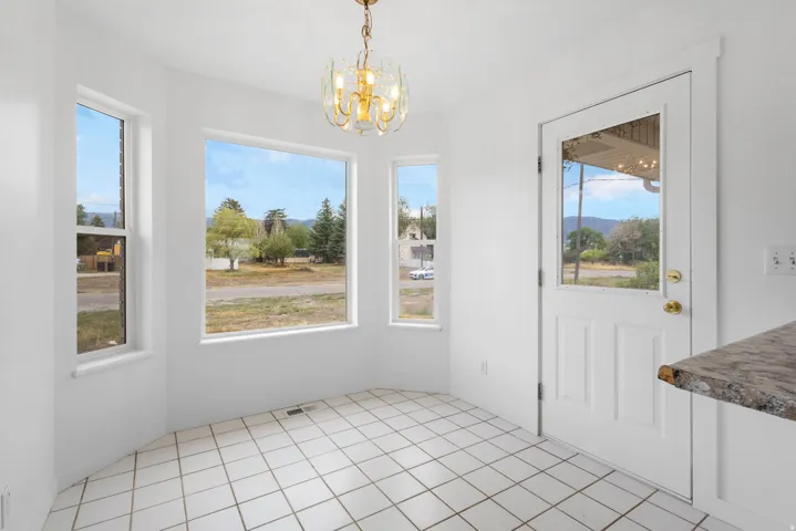 Bay window configuration with multiple windows, contemporary ceiling light fixture, white paneled door with glass insert, white tile flooring, and a stone countertop