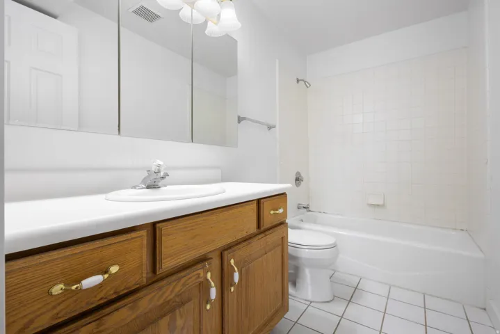 Bathroom featuring a wood-finish vanity with white countertop, integrated sink, and triple mirrored medicine cabinet