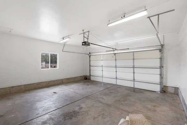 Concrete flooring, horizontal panel garage door, single-pane window, flush-mount fluorescent lighting, and automatic garage door opener