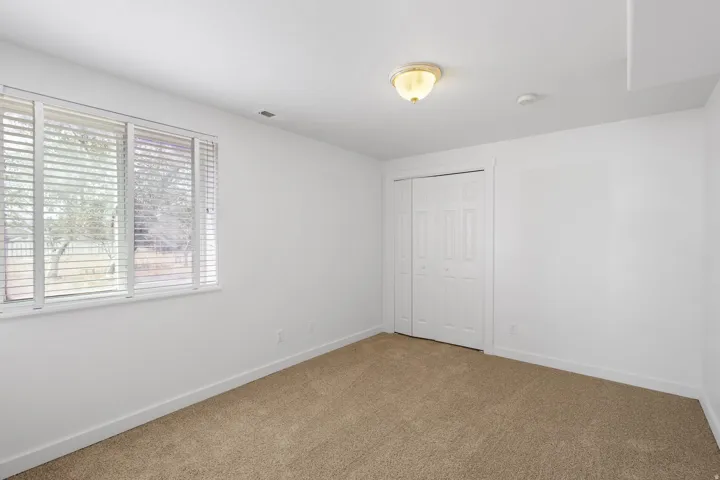 Neutral wall paint, carpeted flooring, window with blinds, bi-fold closet doors, and a ceiling-mounted light fixture