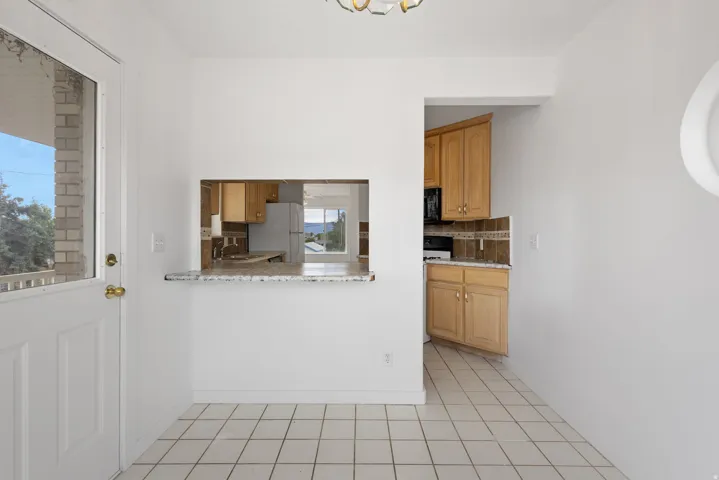 White tile flooring, pass-through opening with stone counter, wood cabinetry, and a full-light exterior door