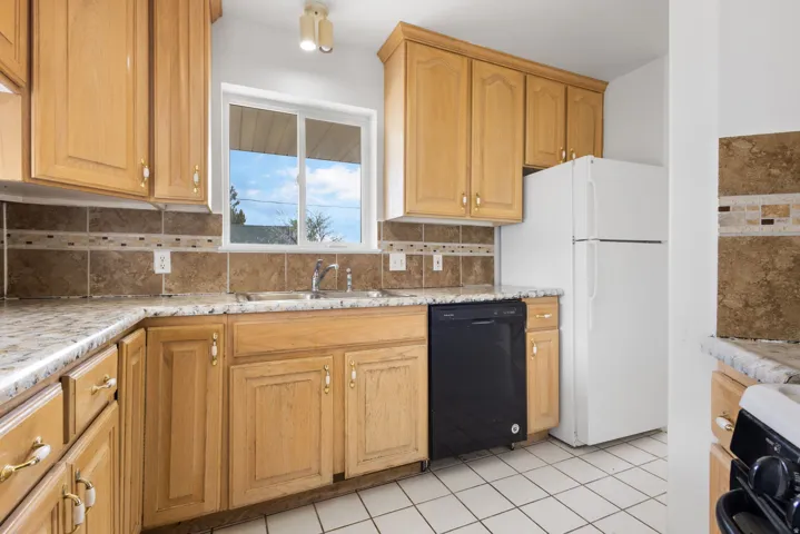Wood-finish cabinetry, tile backsplash with decorative accent, laminate countertops, and white square tile flooring