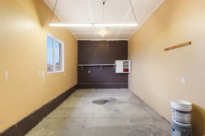 Concrete flooring, wall-mounted shelving, white framed window, permanent overhead lighting, and built-in wall cabinet