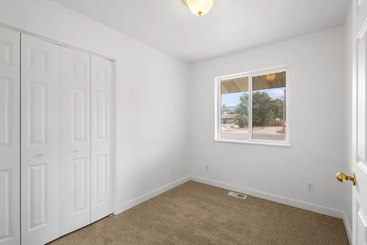 Recessed window with white trim, tan carpeting, and a bi-fold closet