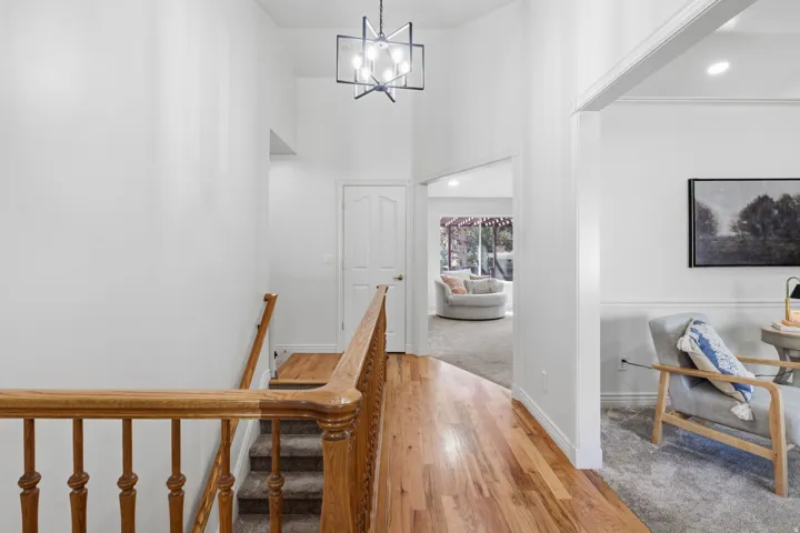 Hardwood flooring, light wood staircase railing, carpeted staircase, vaulted ceiling, and a contemporary chandelier