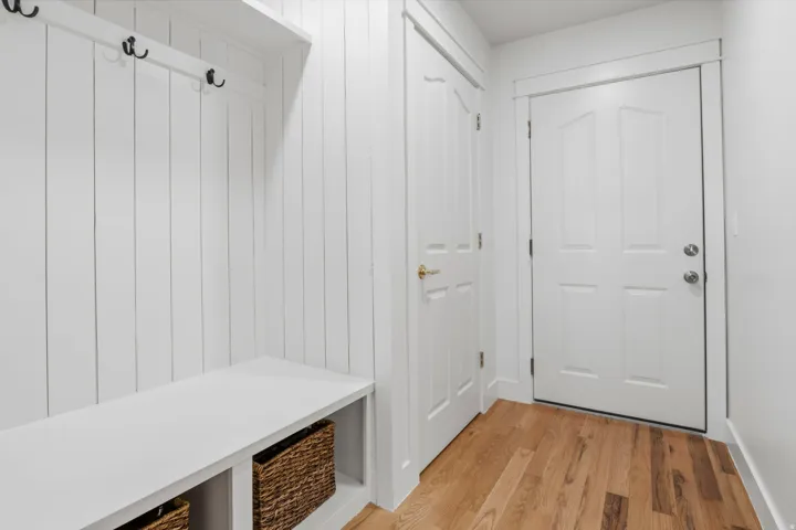 Entryway featuring wood-finish flooring, built-in bench with storage, vertical paneling, and a white paneled door