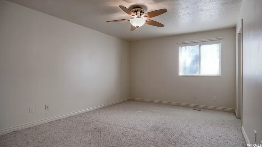 Carpeted flooring with a geometric pattern, neutral wall tones, a ceiling fan with integrated lighting, and a window with blinds
