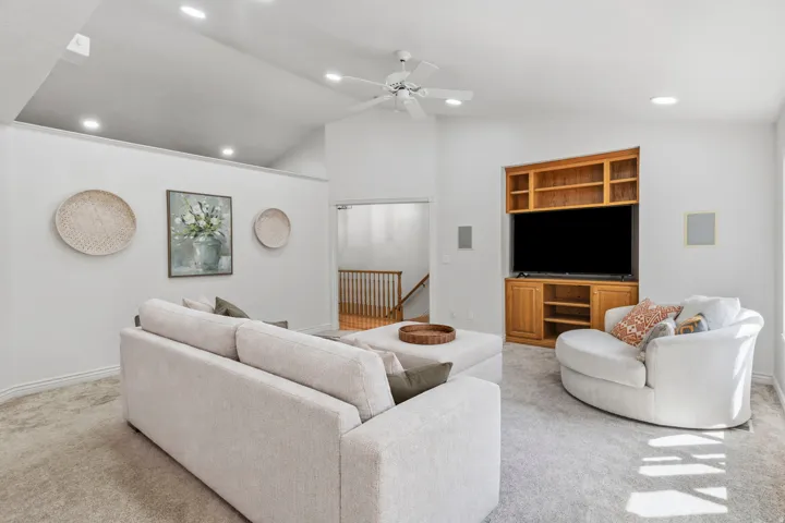Vaulted ceiling with recessed lighting, ceiling fan, built-in entertainment center, and light-toned carpeting