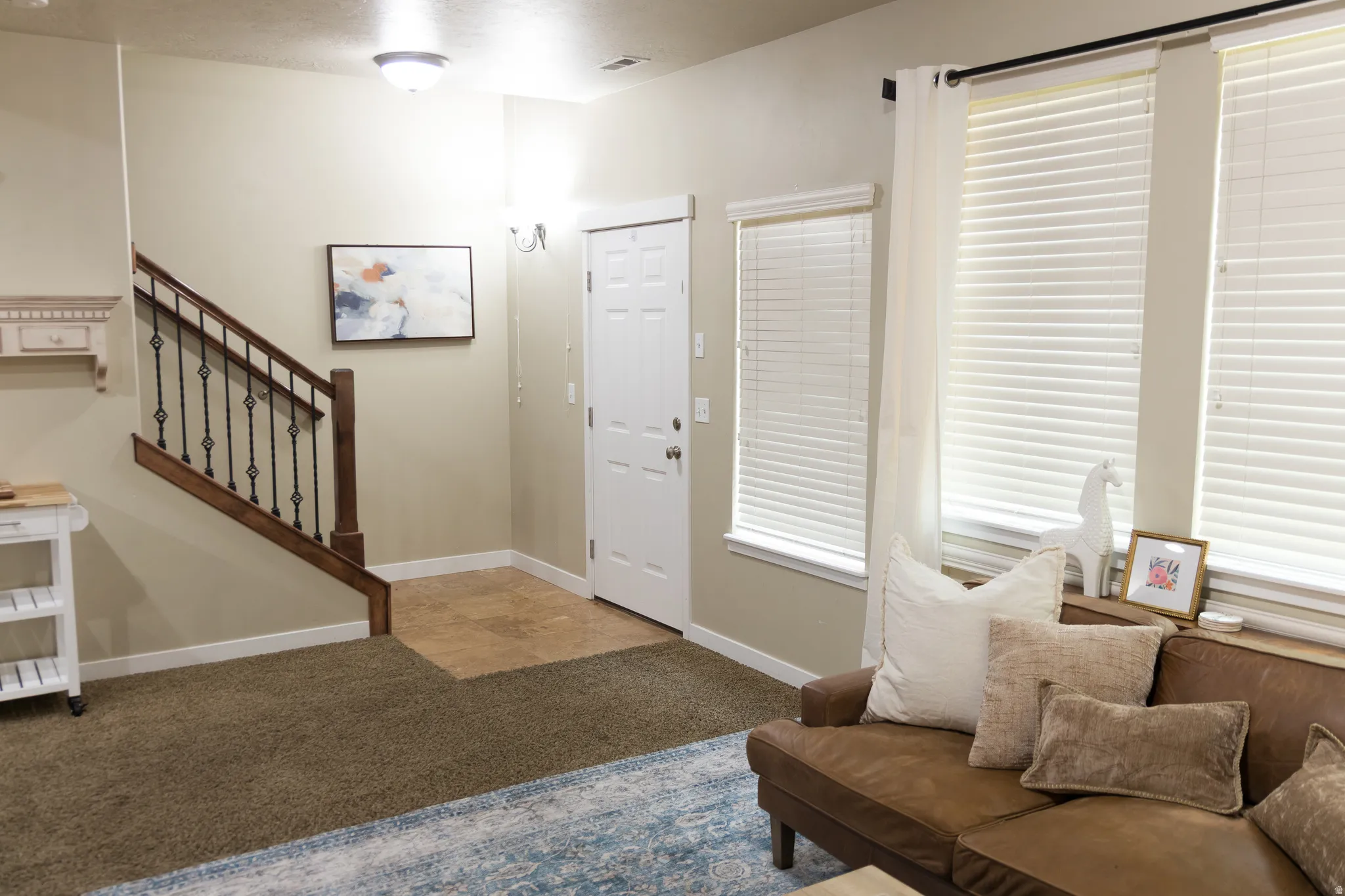 Entryway featuring tile flooring, staircase with wrought iron balusters and wood handrail, and multiple windows with blinds