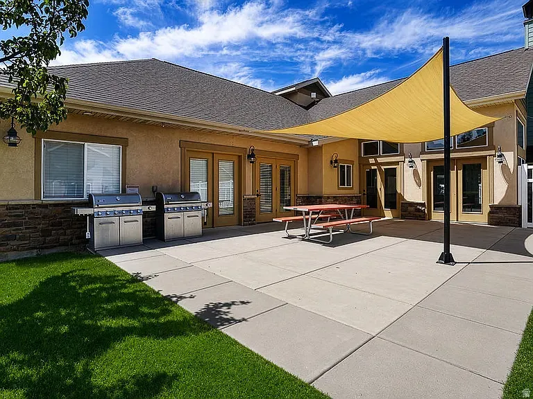 Expansive concrete patio with two built-in grills, a large shade sail, and direct access to interior spaces through multiple glass-paned double doors