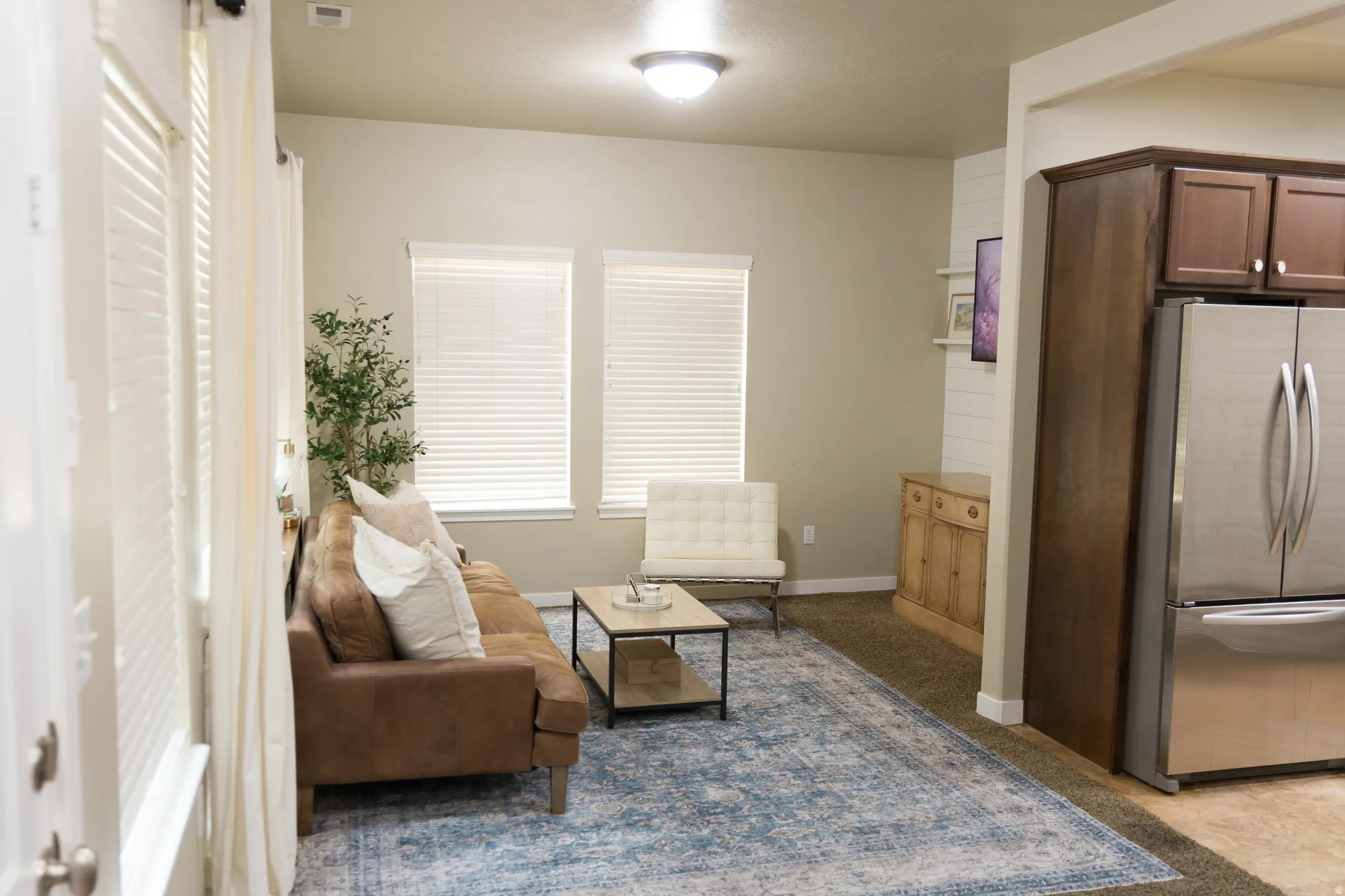 Recessed lighting, warm neutral wall tones, multiple windows with blinds, a built-in wood cabinet, and stainless steel appliances