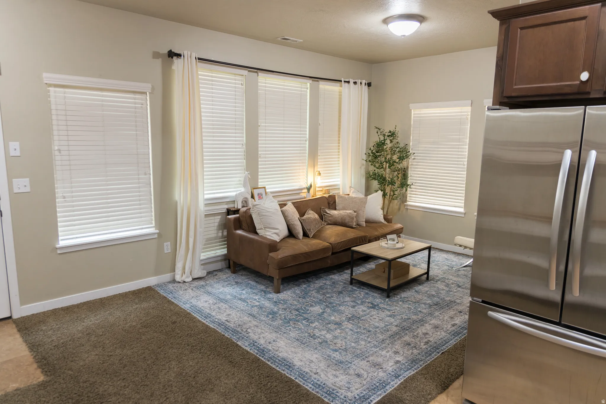 Recessed lighting, multiple windows with blinds, built-in upper cabinetry, and stainless steel refrigerator