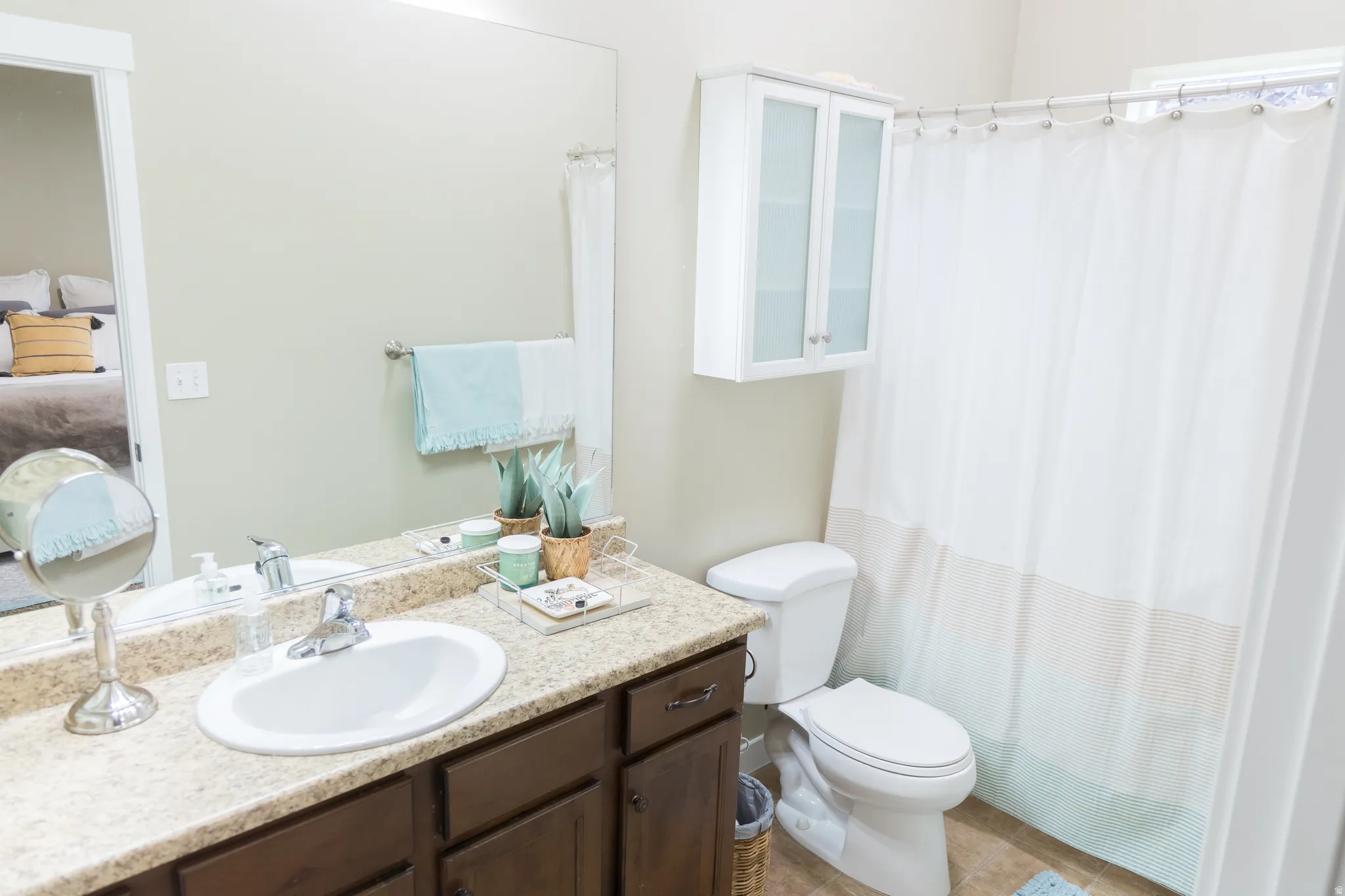 Vanity with a solid surface countertop and undermount sink, dark wood-finish cabinetry, a wall-mounted mirror, and a built-in wall cabinet with frosted glass doors