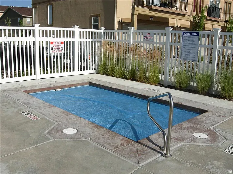 Rectangular spa with a blue cover, surrounded by patterned concrete decking and a white slatted fence