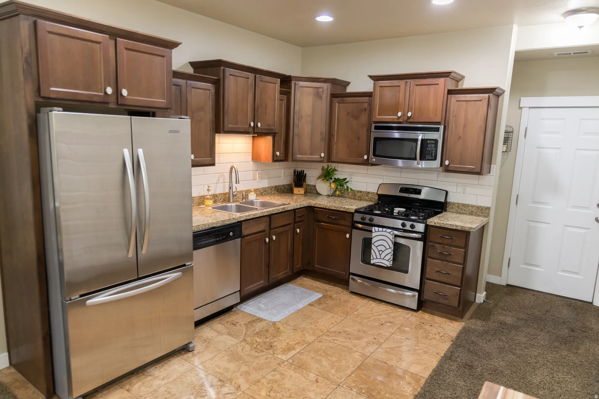Kitchen featuring wood cabinetry, stainless steel appliances, a tile backsplash, light-toned granite countertops, and tile flooring