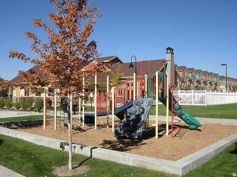Well-appointed community playground featuring a slide, climbing structures, and a wood chip base, bordered by a concrete retaining wall