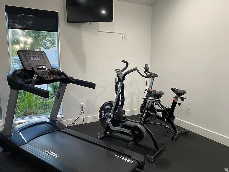 Dedicated fitness space featuring a wall-mounted television, a large window with roller shades, and a durable rubber-finish flooring