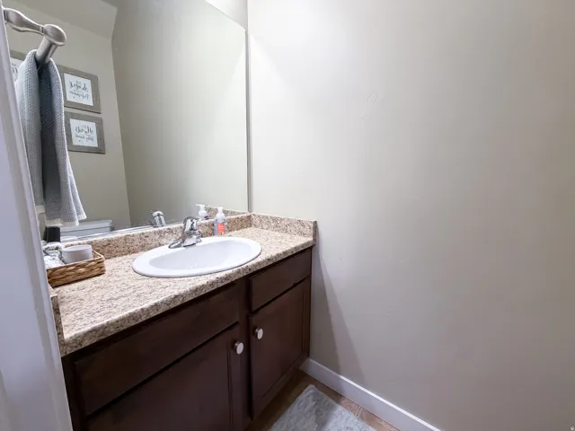 Main level bathroom with granite countertop, integrated white sink, chrome faucet, and dark wood-finish cabinetry