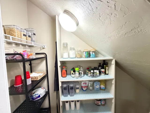 Recessed pantry with built-in shelving, overhead lighting, and angled ceiling
