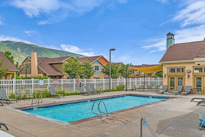 Outdoor swimming pool with concrete surround, perimeter fencing, and an adjacent building featuring multiple glass-paned doors