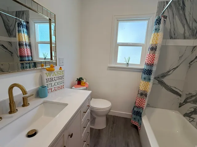 Bathroom featuring a built-in vanity with a white countertop and integrated sink, gold-finish faucet, framed mirror, and a window