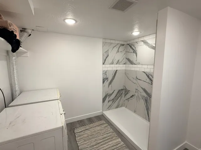 Walk-in shower with large-format marbled tile, recessed shelving, and a subway tile accent band
