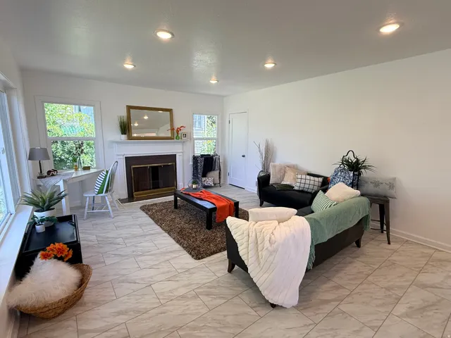 Recessed lighting illuminates this living space featuring a fireplace with a white mantel, multiple windows, and light-toned tile flooring