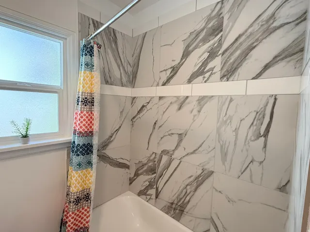 Bathtub with full-height wall tiling, featuring large format tiles with a veined pattern and a white subway tile accent