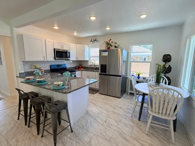 Open-concept kitchen featuring white cabinetry, stainless steel appliances, granite countertops, a subway tile backsplash, and recessed lighting
