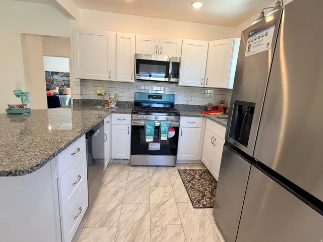 Kitchen featuring granite countertops, white shaker cabinetry, a subway tile backsplash, stainless steel appliances, and tiled flooring