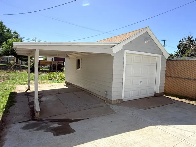 Detached garage with horizontal siding, a single garage door, and an attached carport