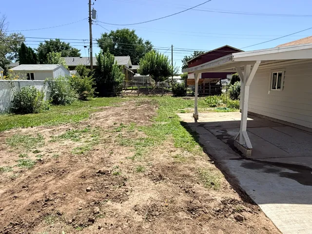 Carport structure with a concrete pad, a chain link fence, and a partially grassed and exposed earth yard area