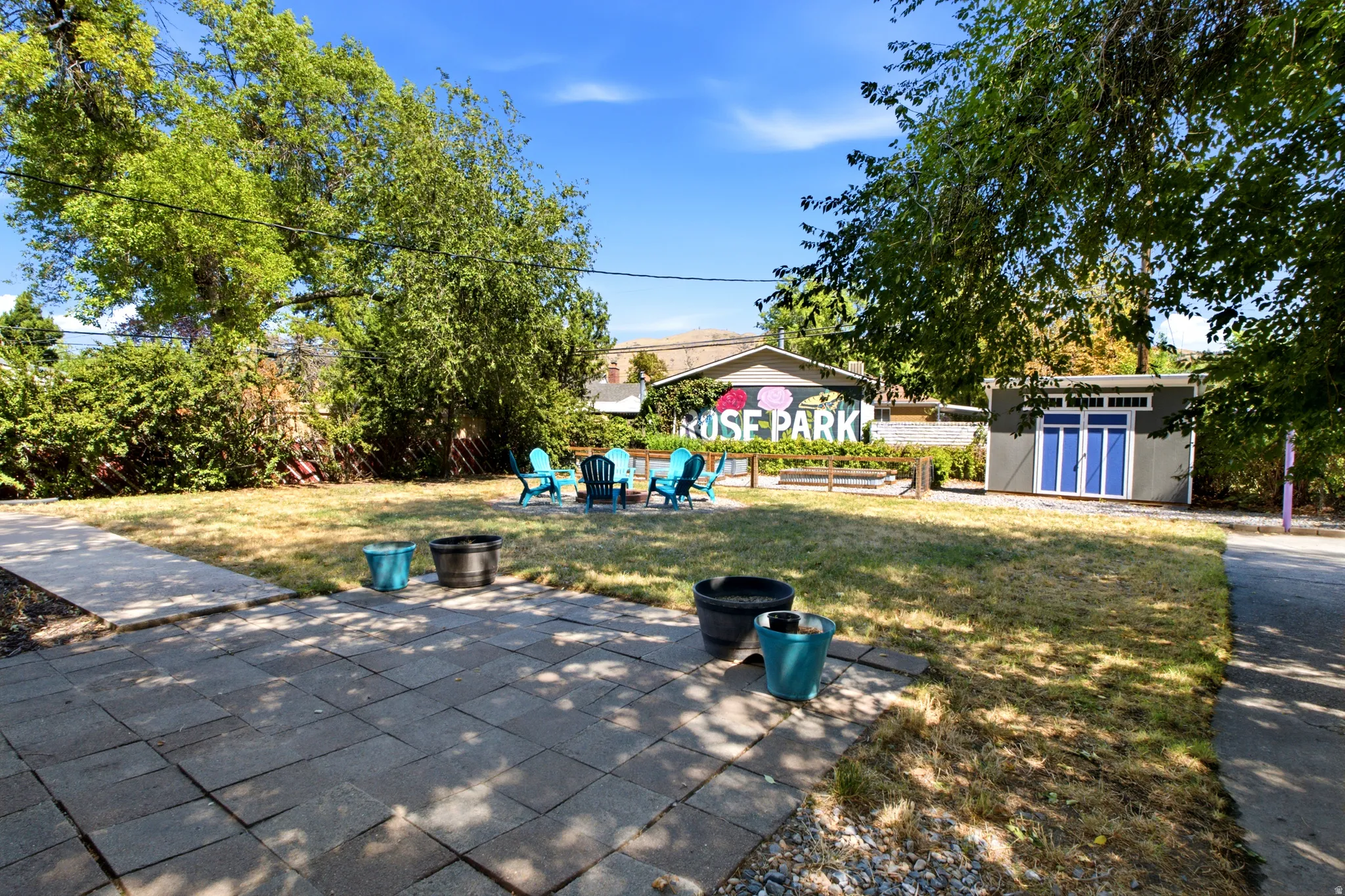 Expansive backyard featuring a patio, mature trees, and a detached storage shed with blue doors