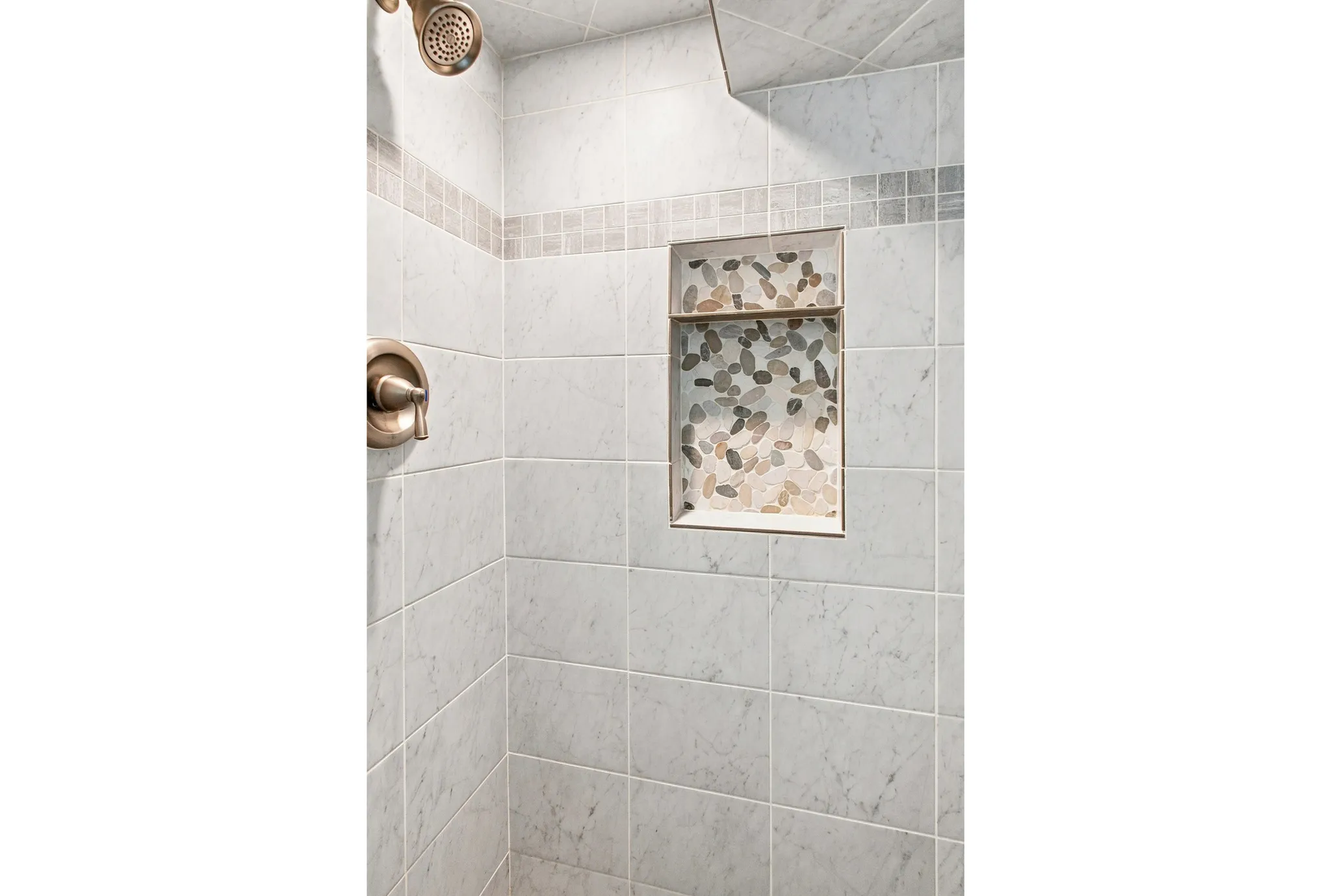 Subway tile shower with recessed niche with pebble tile, and a brushed nickel shower fixture