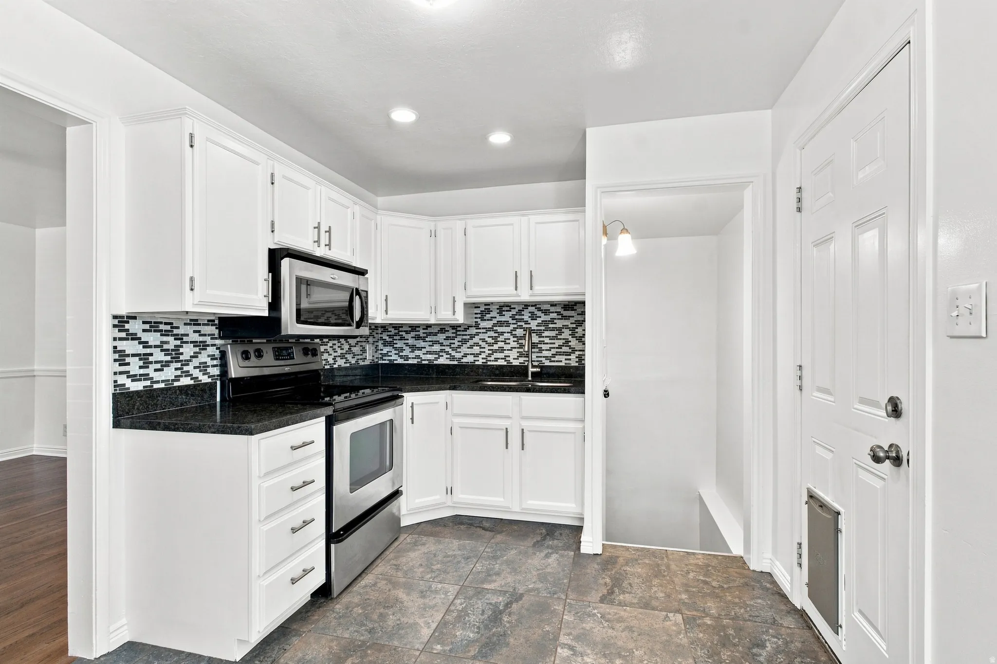 White cabinetry with stainless steel appliances, dark countertops, and mosaic tile backsplash