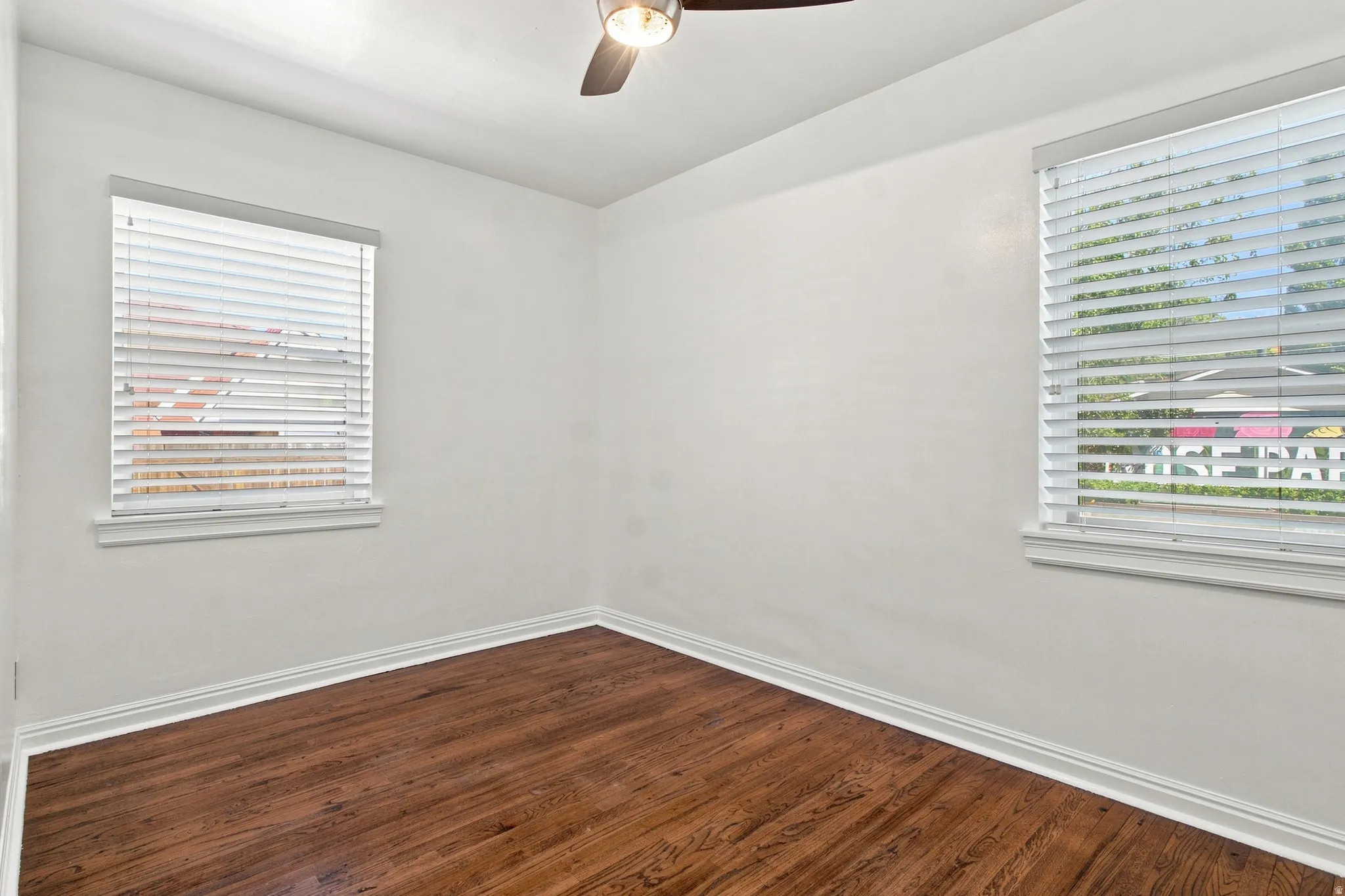 Hardwood flooring, two windows with blinds, ceiling fan with integrated lighting, and white trim throughout