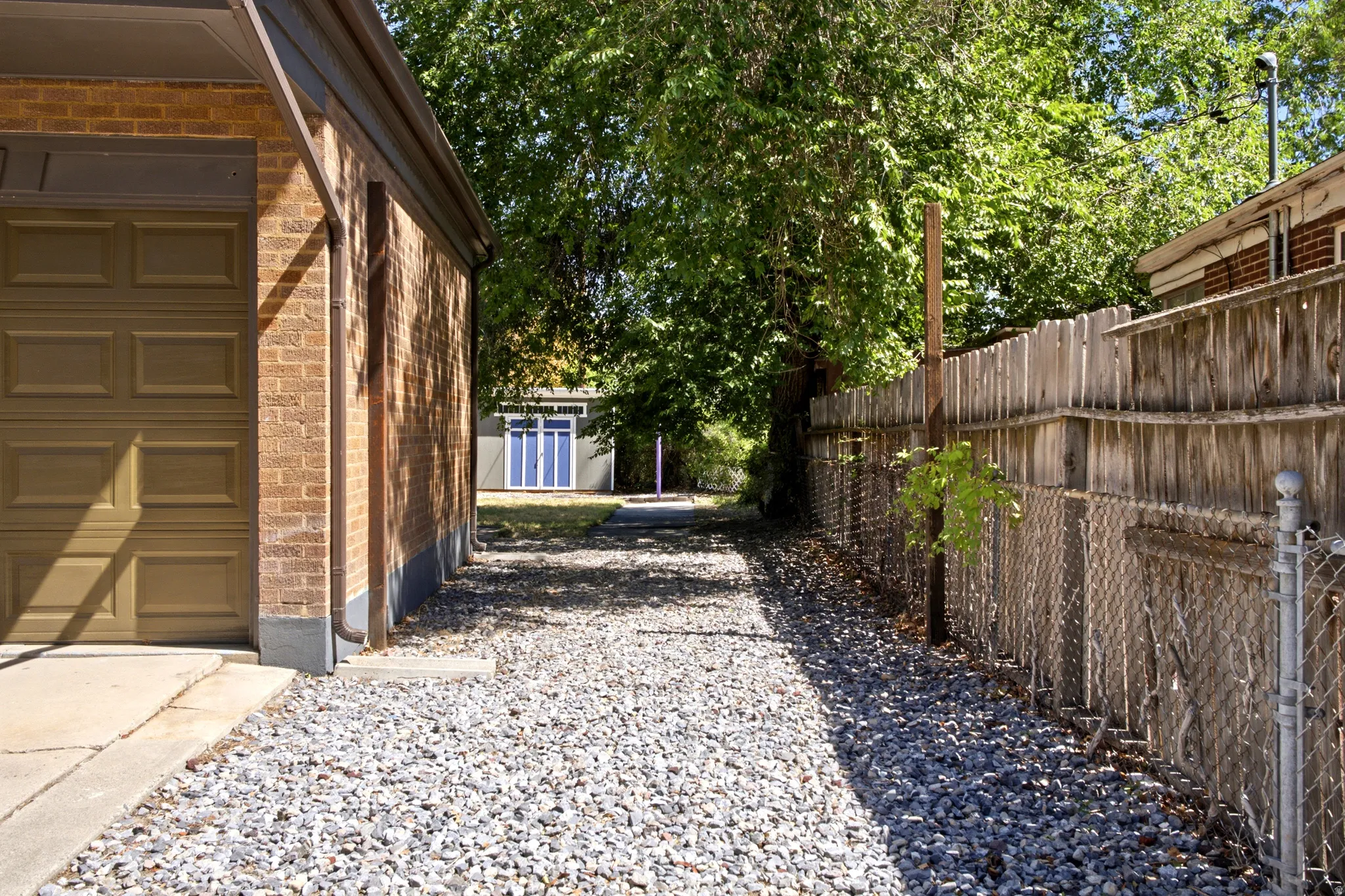 Brick exterior with a garage door, gravel RV parking, and wood fencing