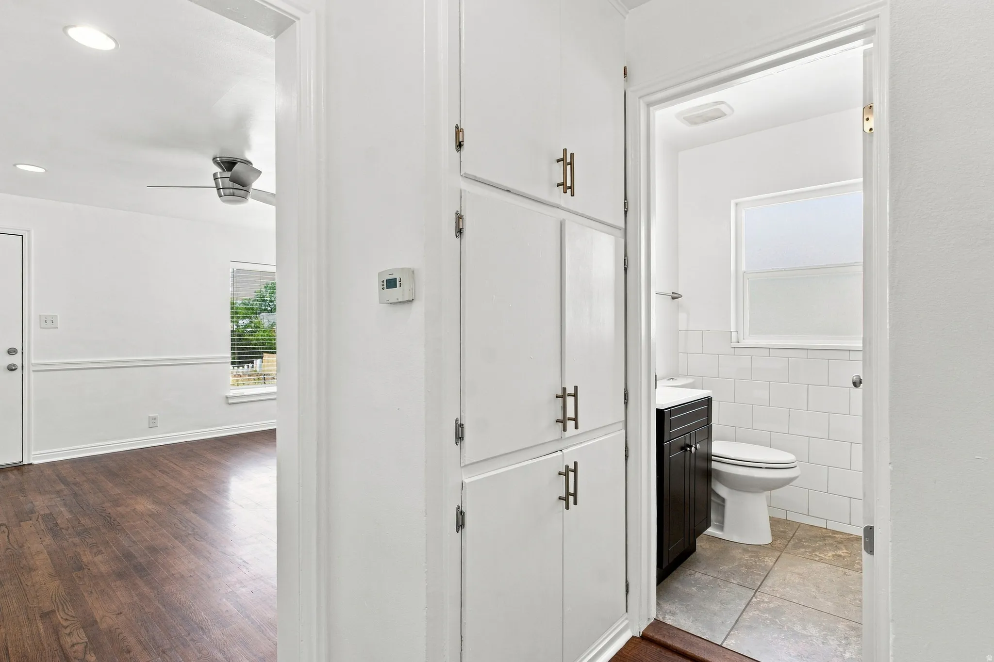 Built-in hallway storage with brushed nickel hardware, wood-finish flooring, ceiling fan, and a bathroom featuring subway tile and a dark wood-finish vanity