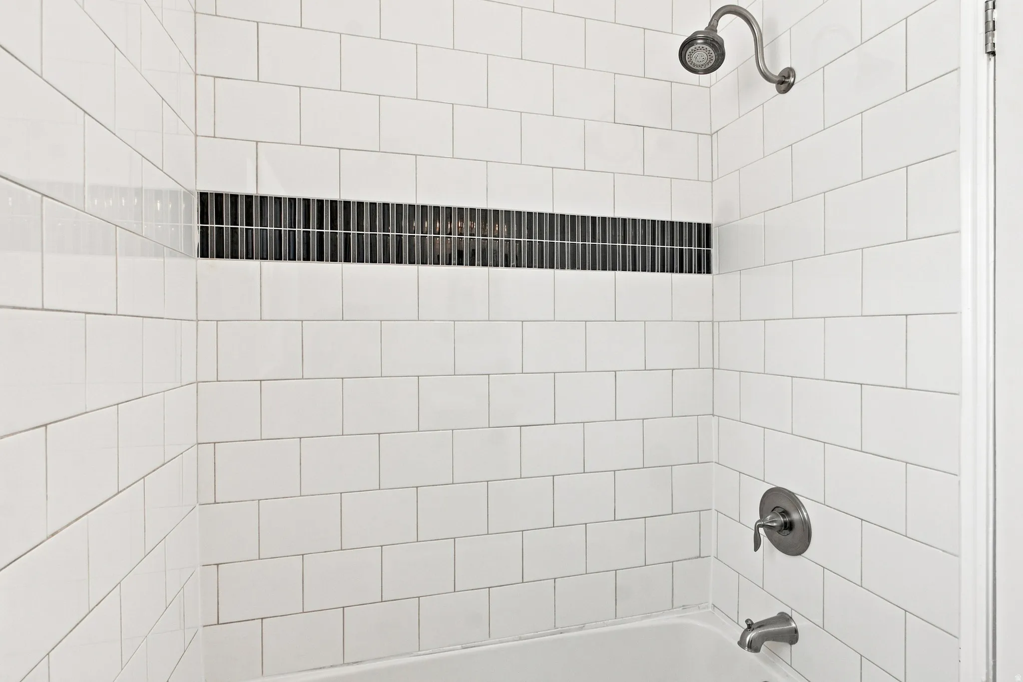 White subway tile surround with a dark tile accent band, brushed nickel showerhead and faucet, and white bathtub