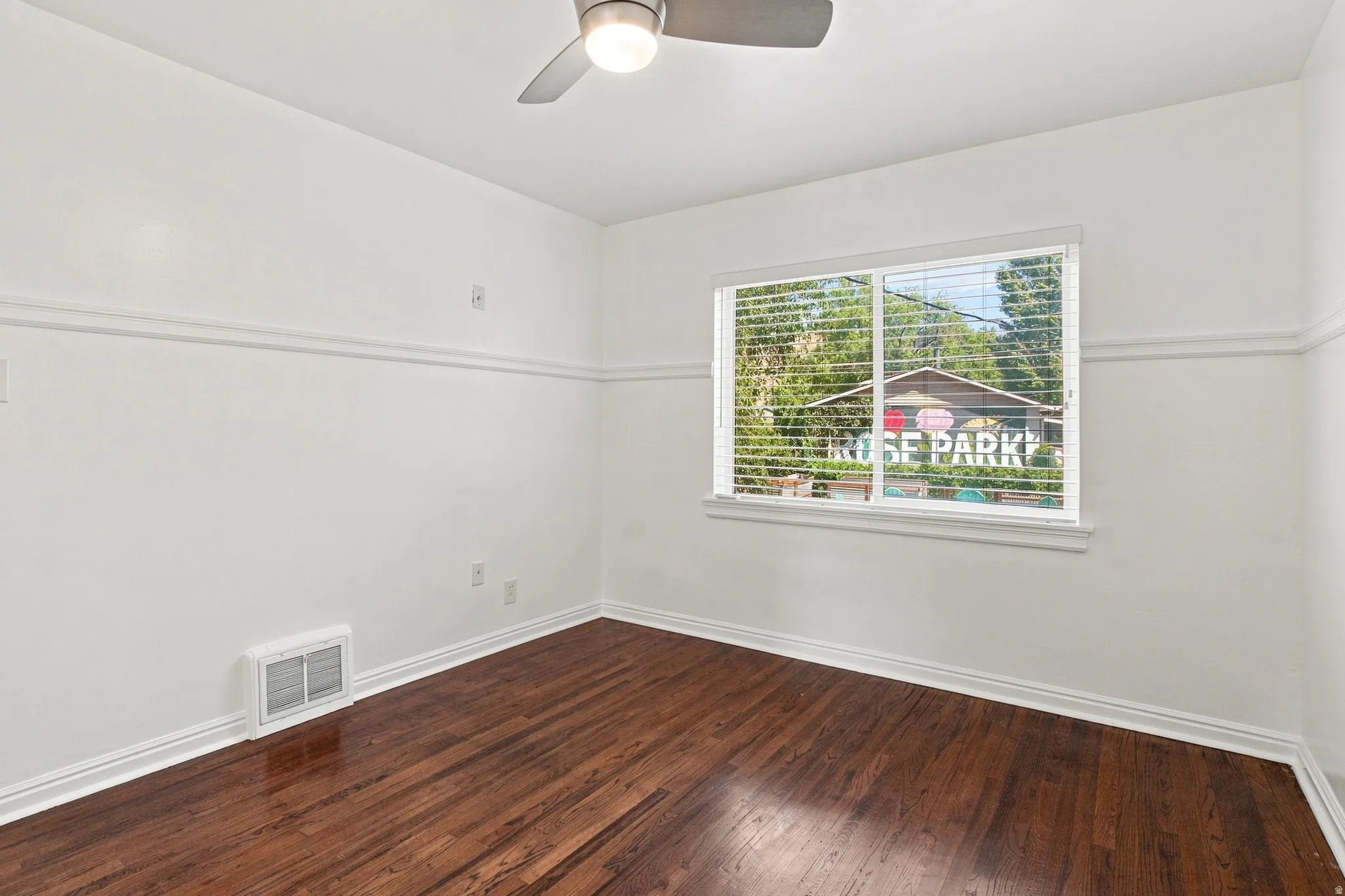 Hardwood-finish flooring, crisp white walls with chair rail molding, ceiling fan with integrated lighting, and a window featuring blinds
